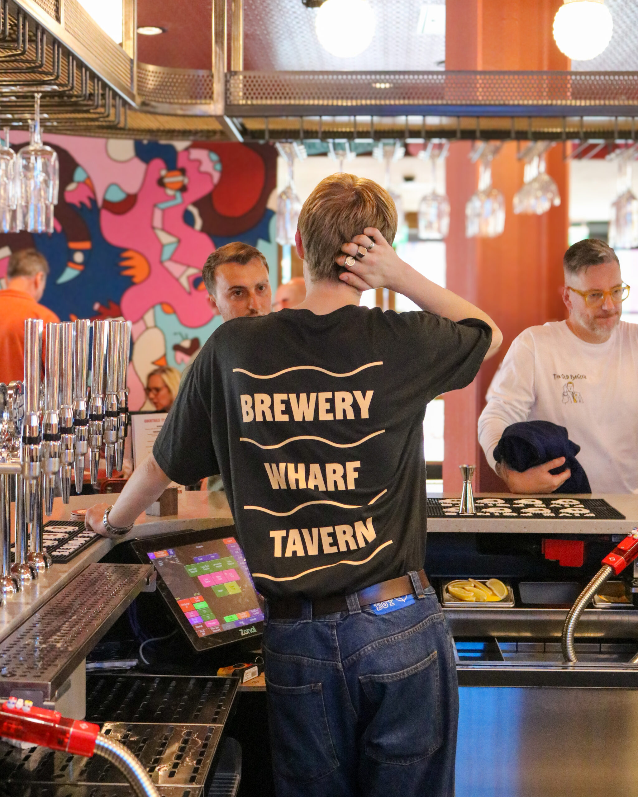 a person behind a bar with a tshirt saying brewery wharf tavern