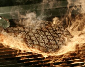 a beef steak on a grill surrounded by fire