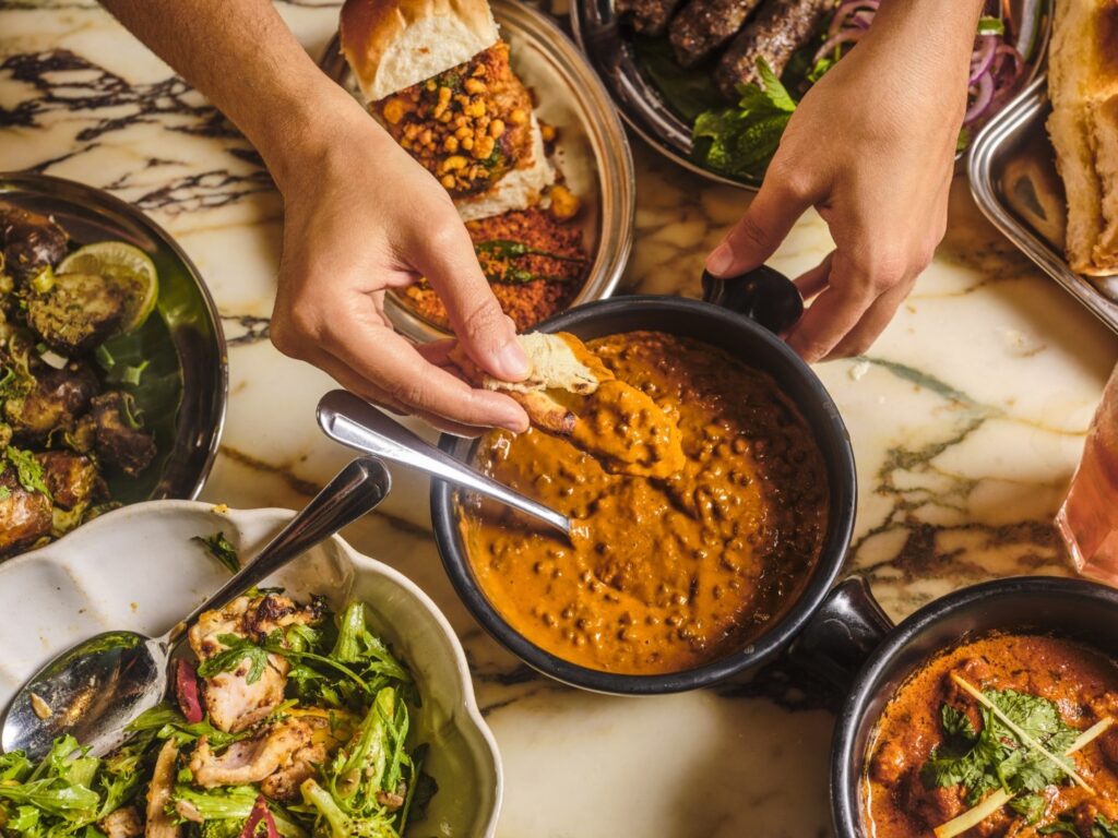 several plates of food, curry and vegetab;es with someone holding one in the middle