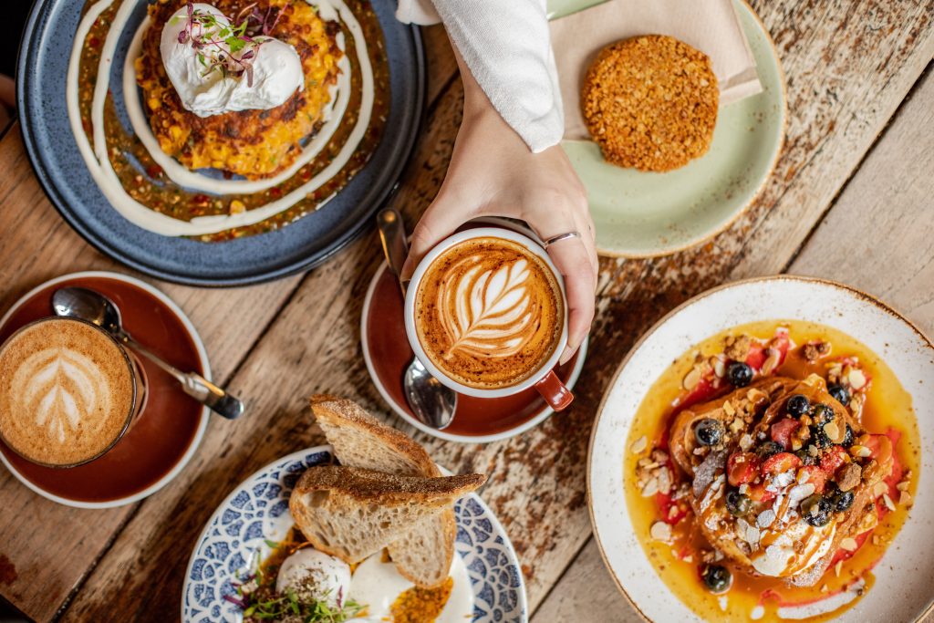 a table with several plates laid out with breakfast foods like pancakes and toast and a coffee in the middle