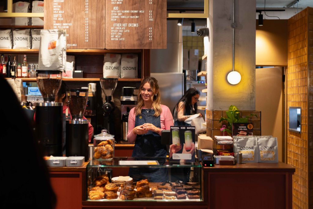 a cafe setting with baked goods in a glass counter and someone in an apron serving