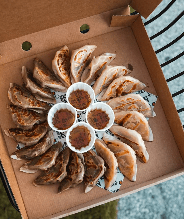 a takeaway box with gyozas in a circle with a dipping sauce in the middle