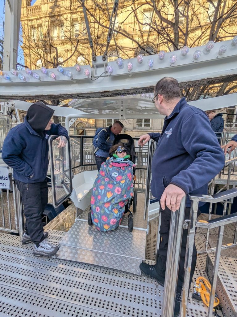 someone in a wheelchair being escorted onto a accessible gondola in a ferris wheel