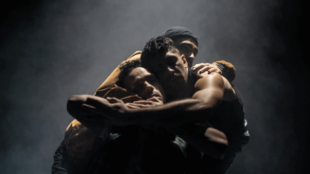 three people in low lighting holding each other tightly