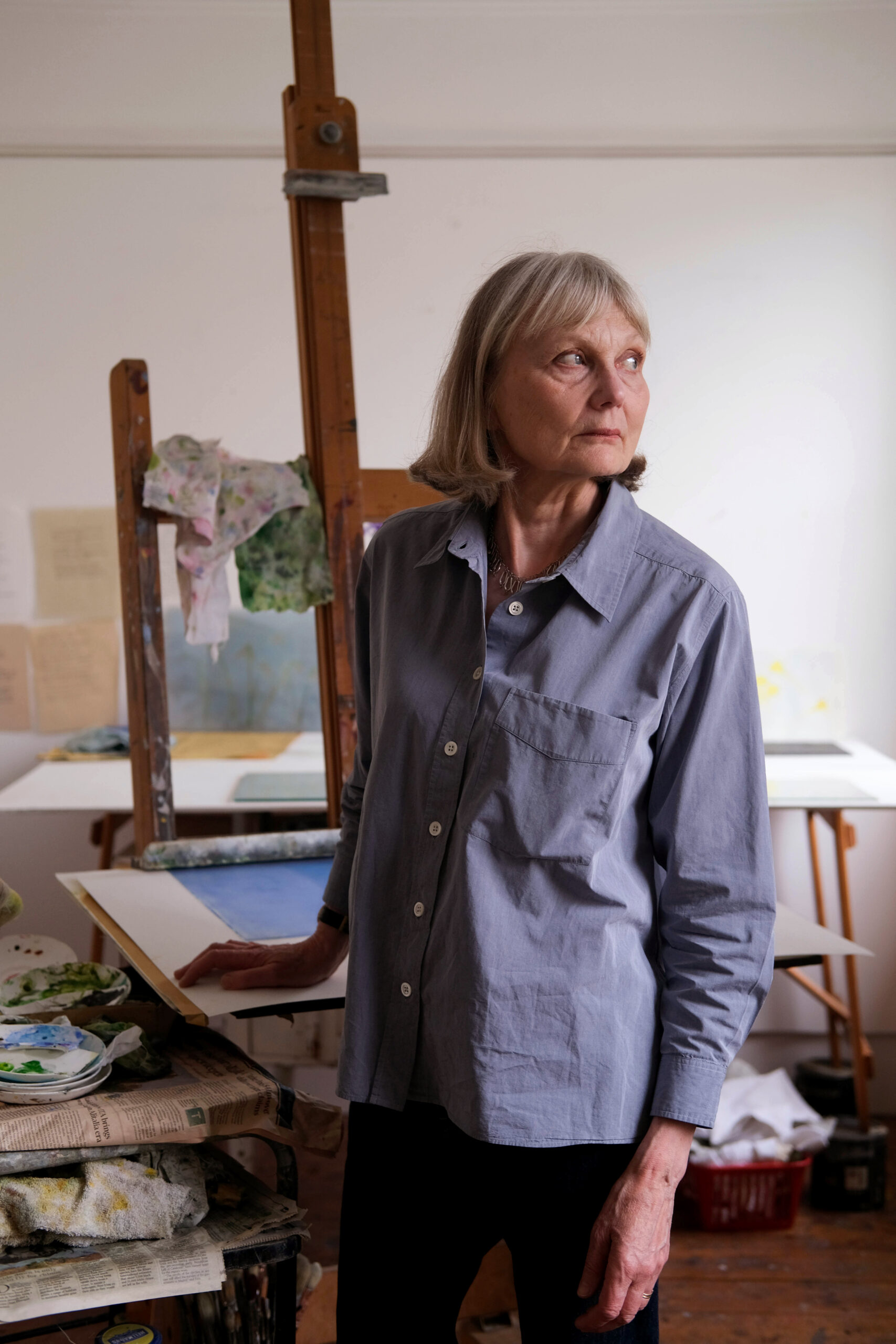 a woman stood in front of an easel with a painting on it and other paintings further behind