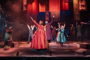 several actors on a stage in bright colourful Victorian outfits dancing