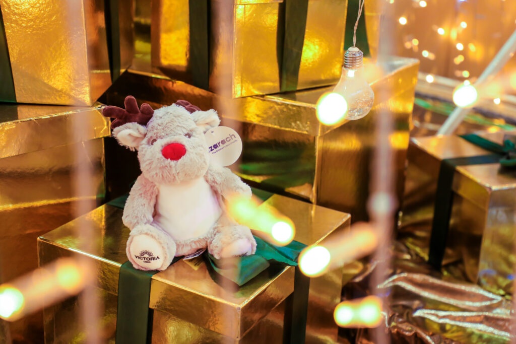 a plush teddy of a reindeer sat on a gold present box with fairy lights around it