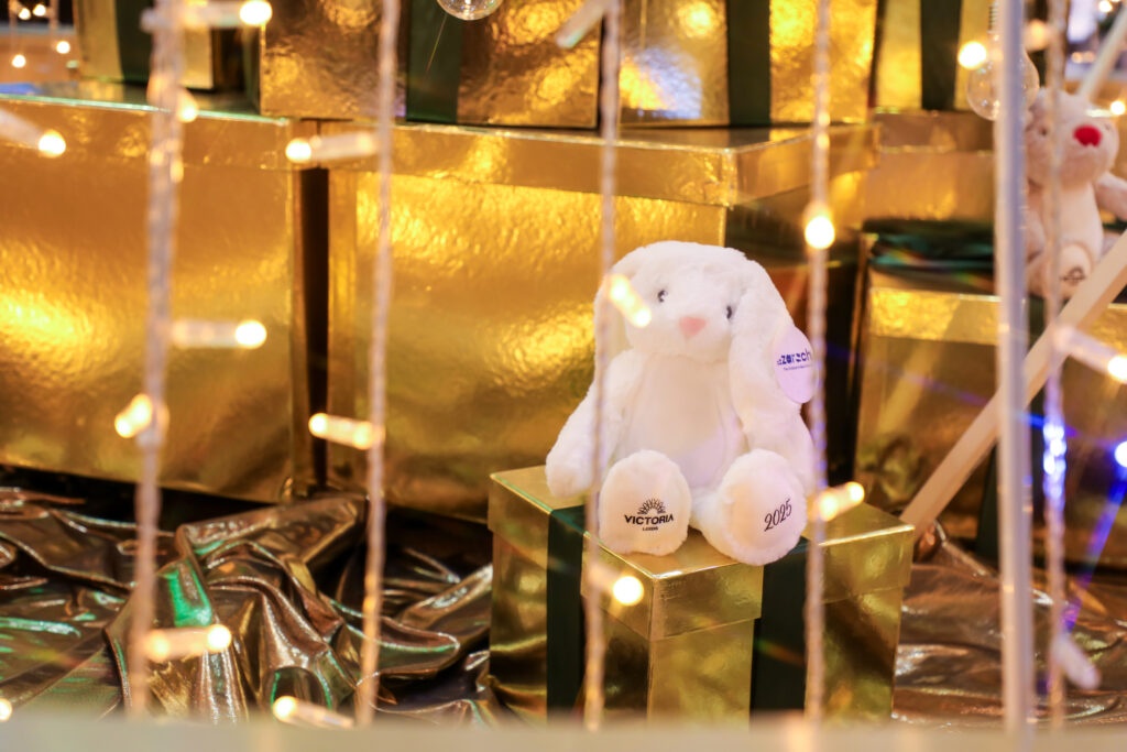 a plush teddy of a snow hare sat on a gold present box with fairy lights around it