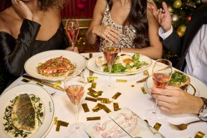 a table laid out with plates of food, champagne glasses and gold confetti and people sat around