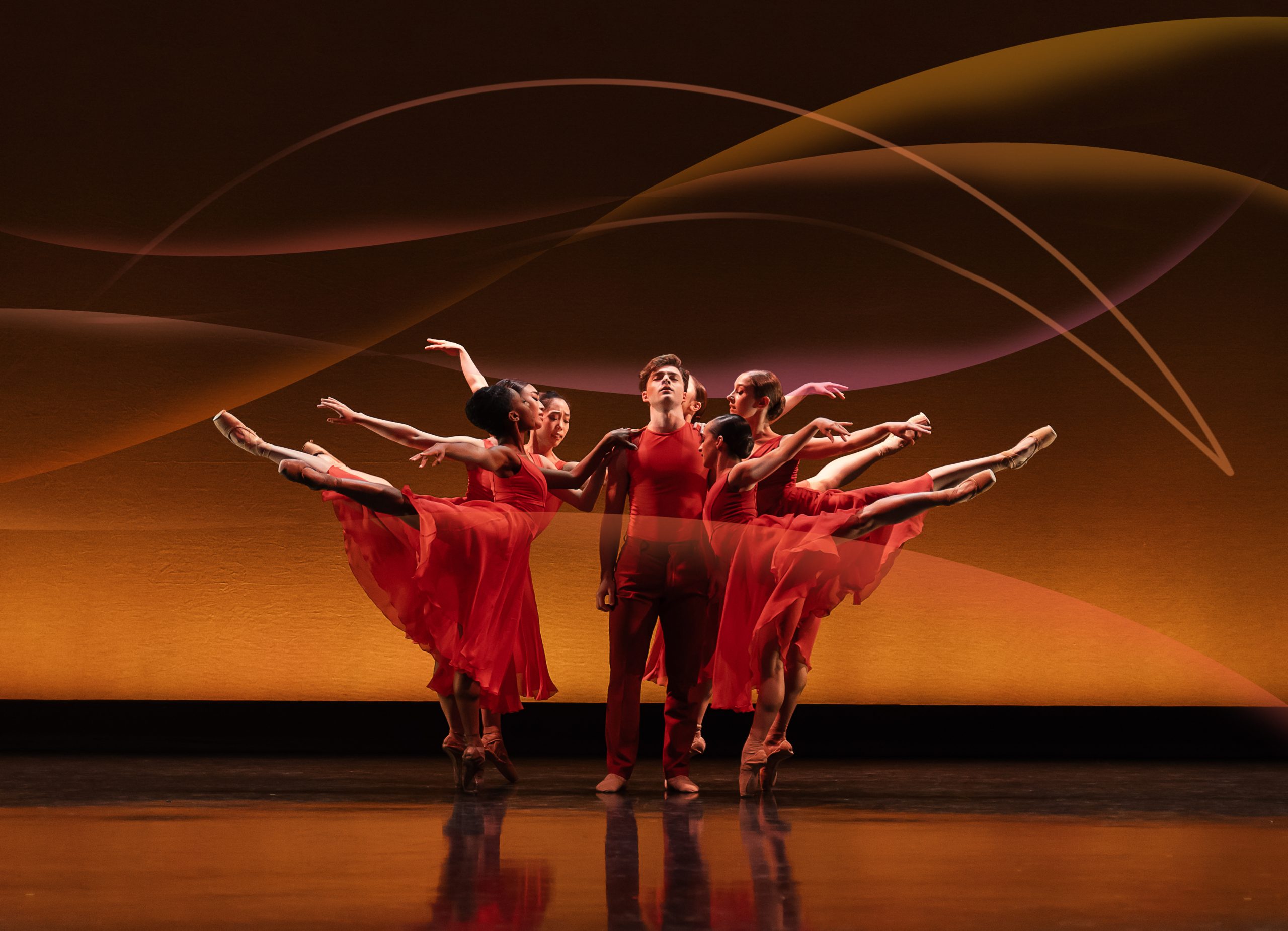 several ballet dancers in a circle on a stage in red flowing outfits