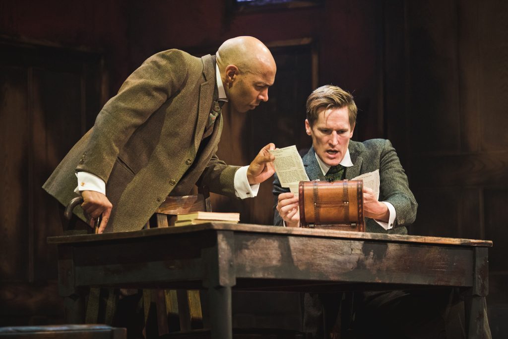 two men exploring an open box on a table with papers in it
