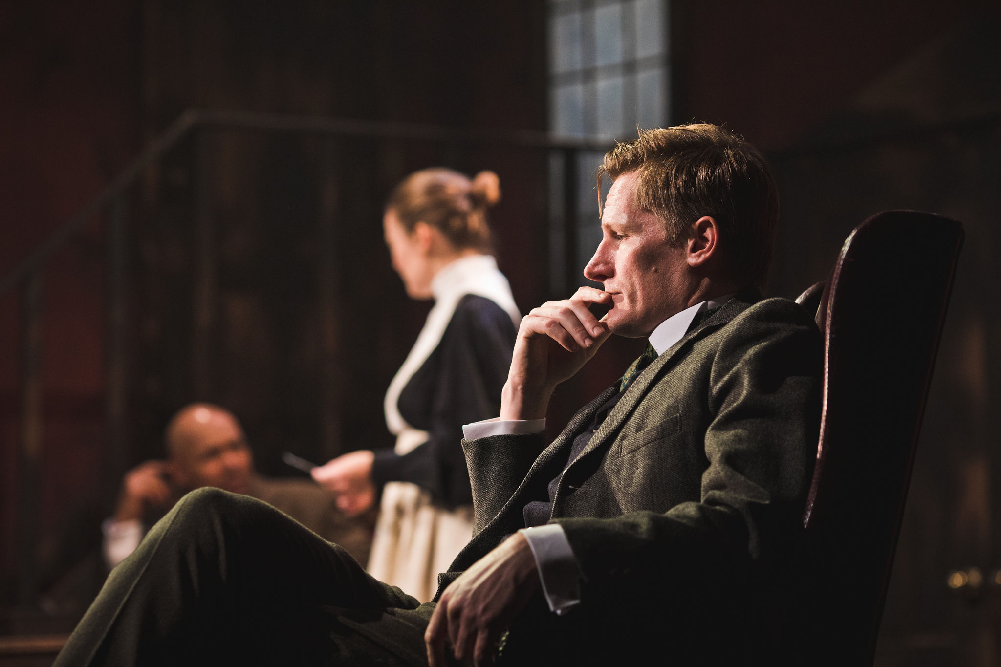 a man sat looking in thought whilst someone is in the background