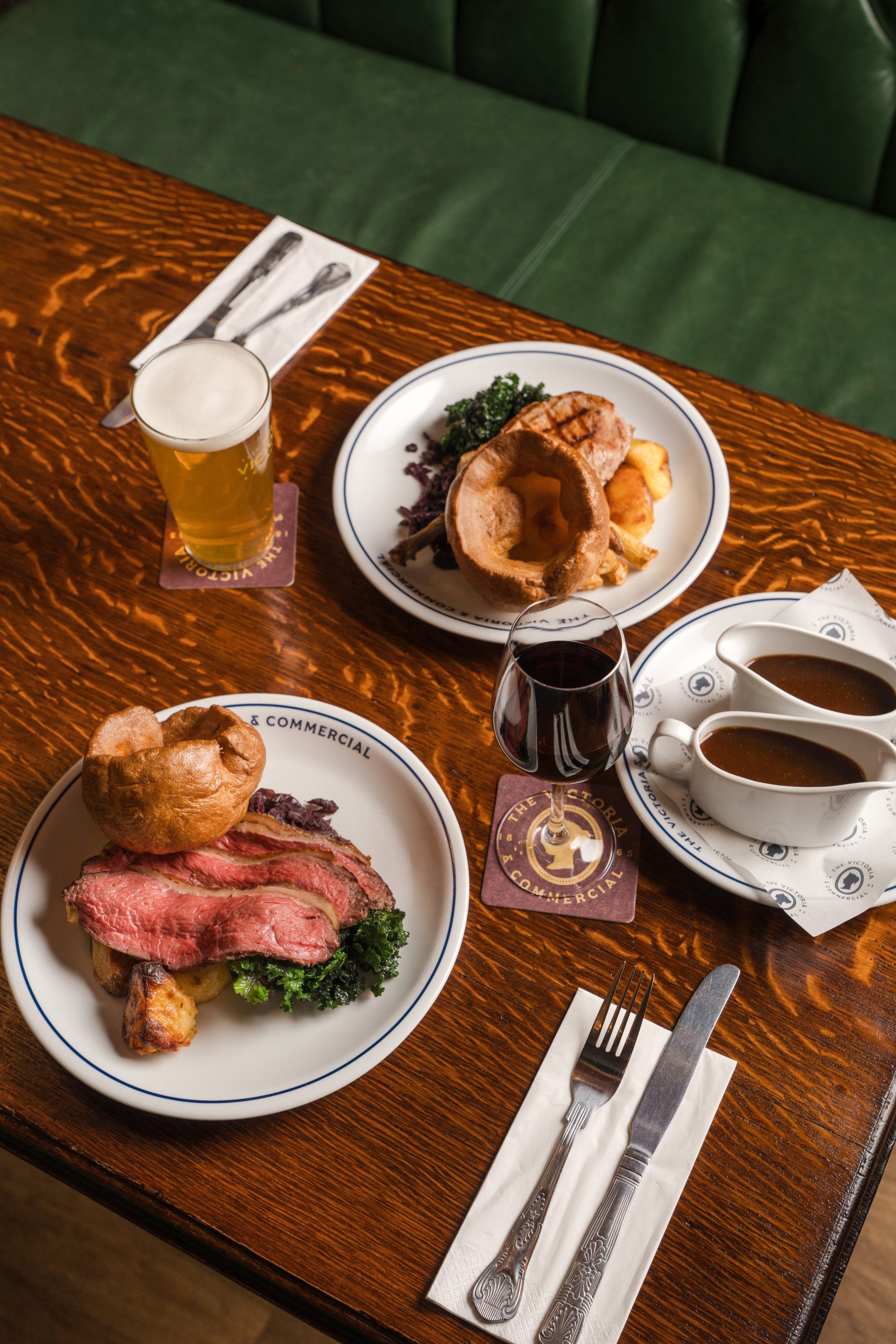 a wooden table with two roast dinners laid out with yorkshire puddings, two boats of gravy, a pint of beer and a glass of wine