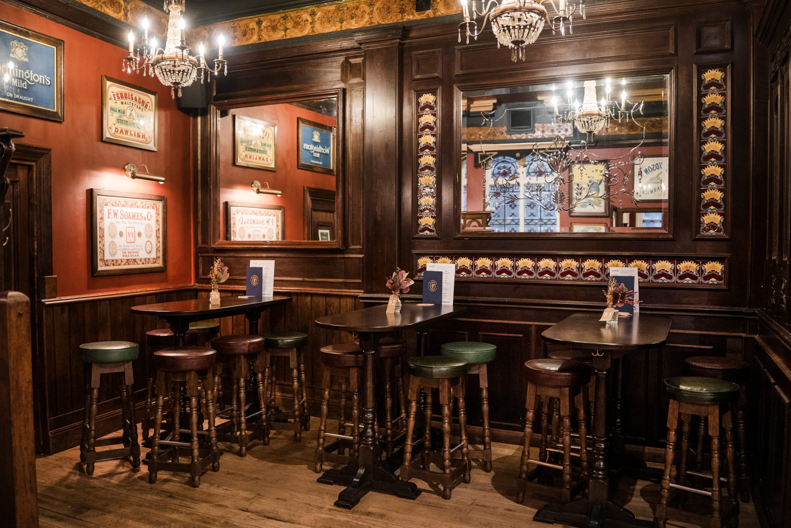 a traditional old pub setting with wooden tables, chairs, floors and walls all in warm tones, mirrors on the walls and glass chandeliers