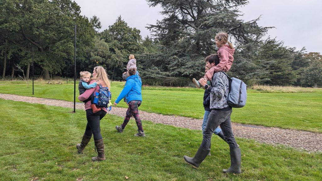 a family of parents and small children walking in a field with trees behind them