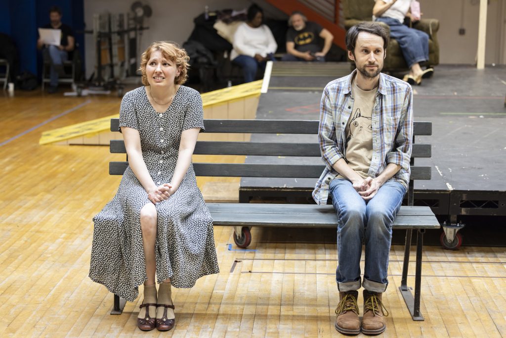 two people at a theatre rehearsal, sat on a bench
