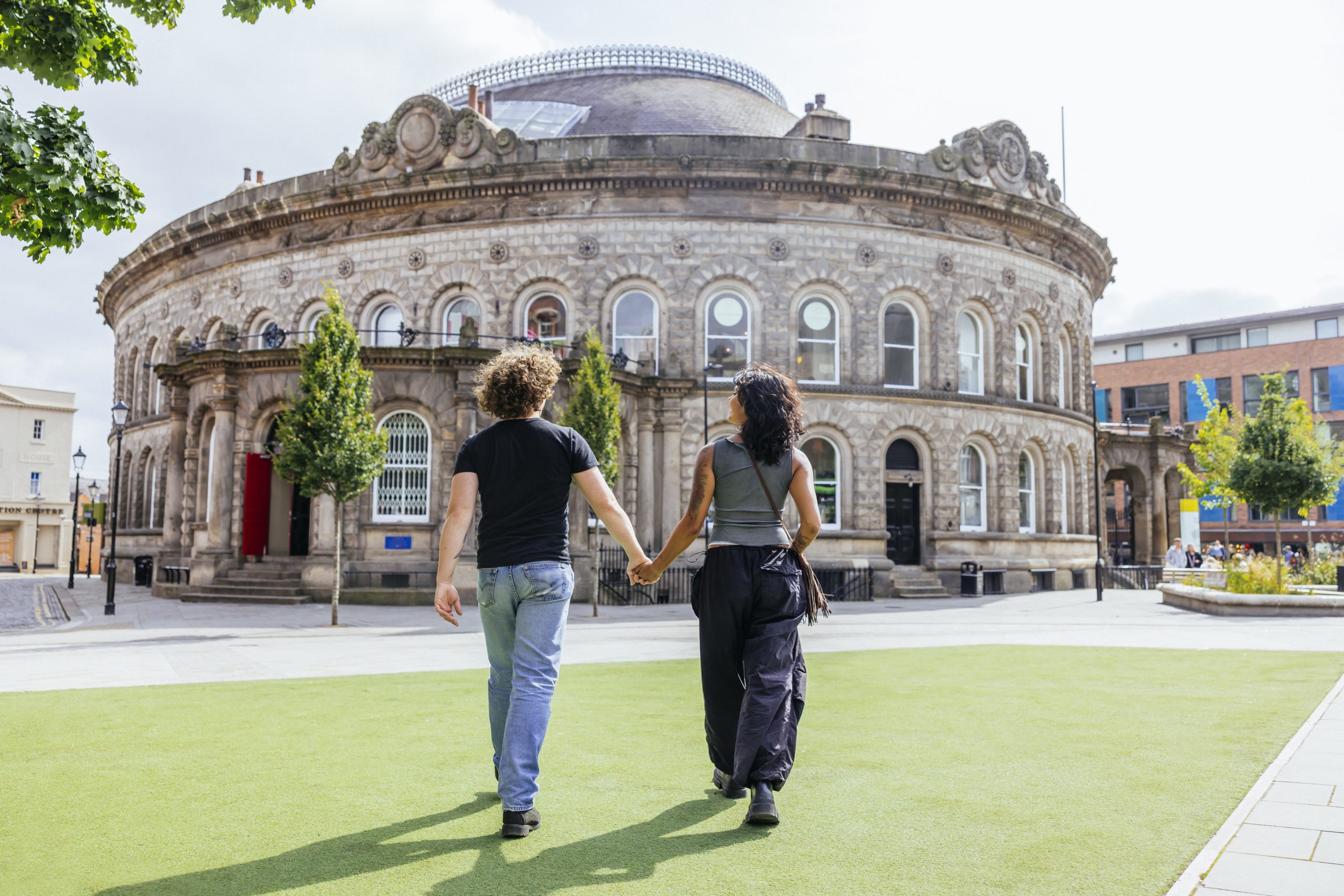 a young couple walking holding hands towards a large circular brick building