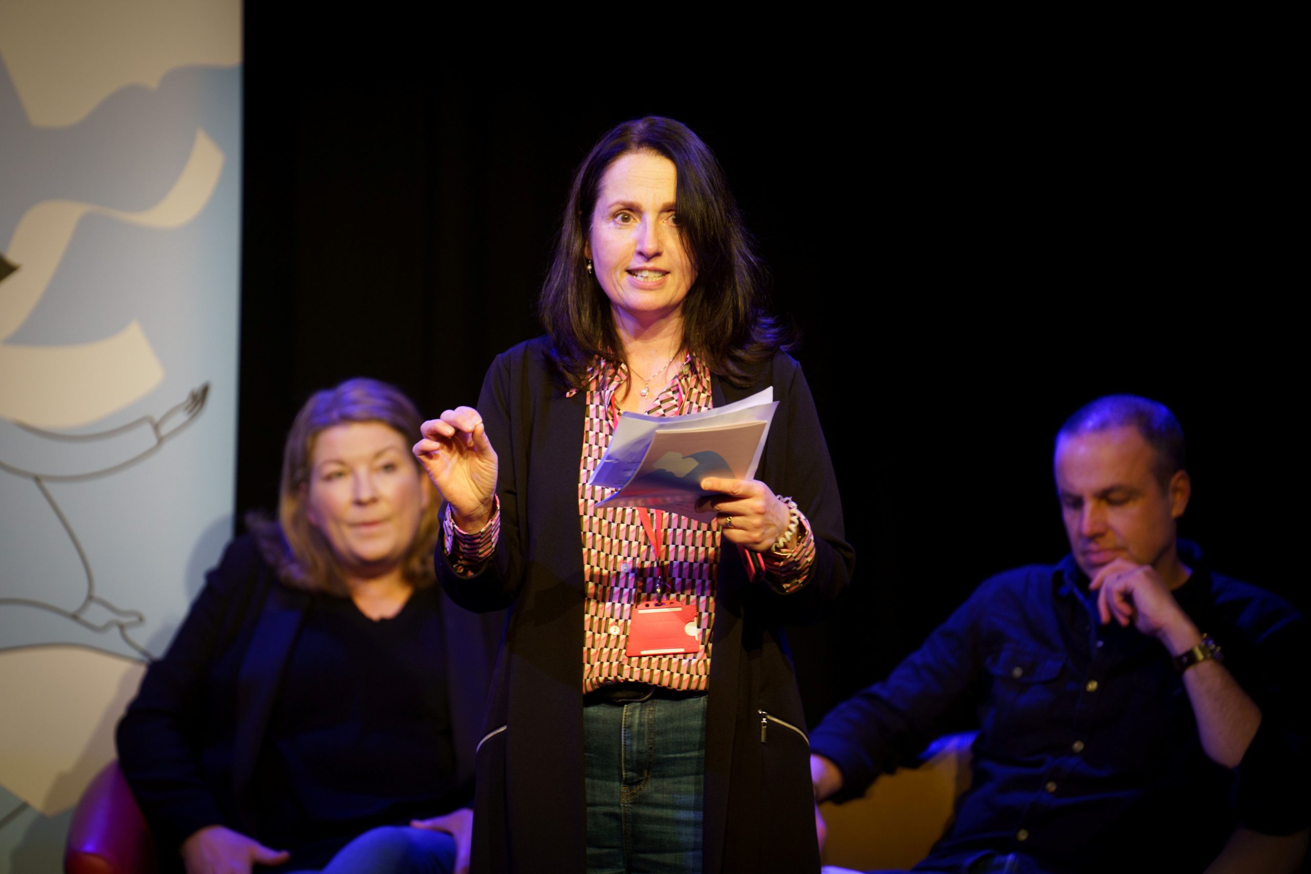 a person stood up holding a book and reading aloud to a crowd of people