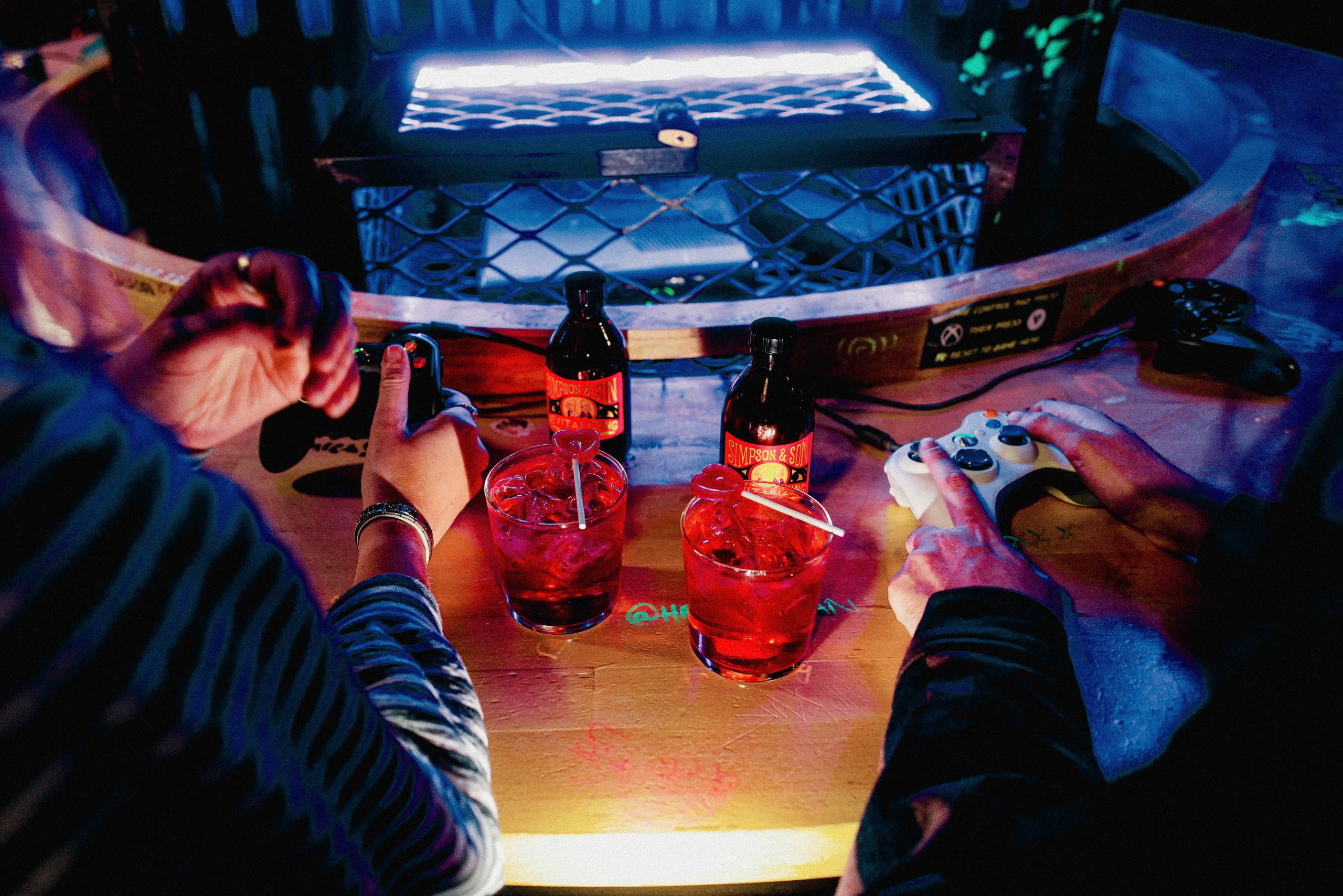 two people holding game controllers with matching cocktails with heart lollipops in front of them in a table