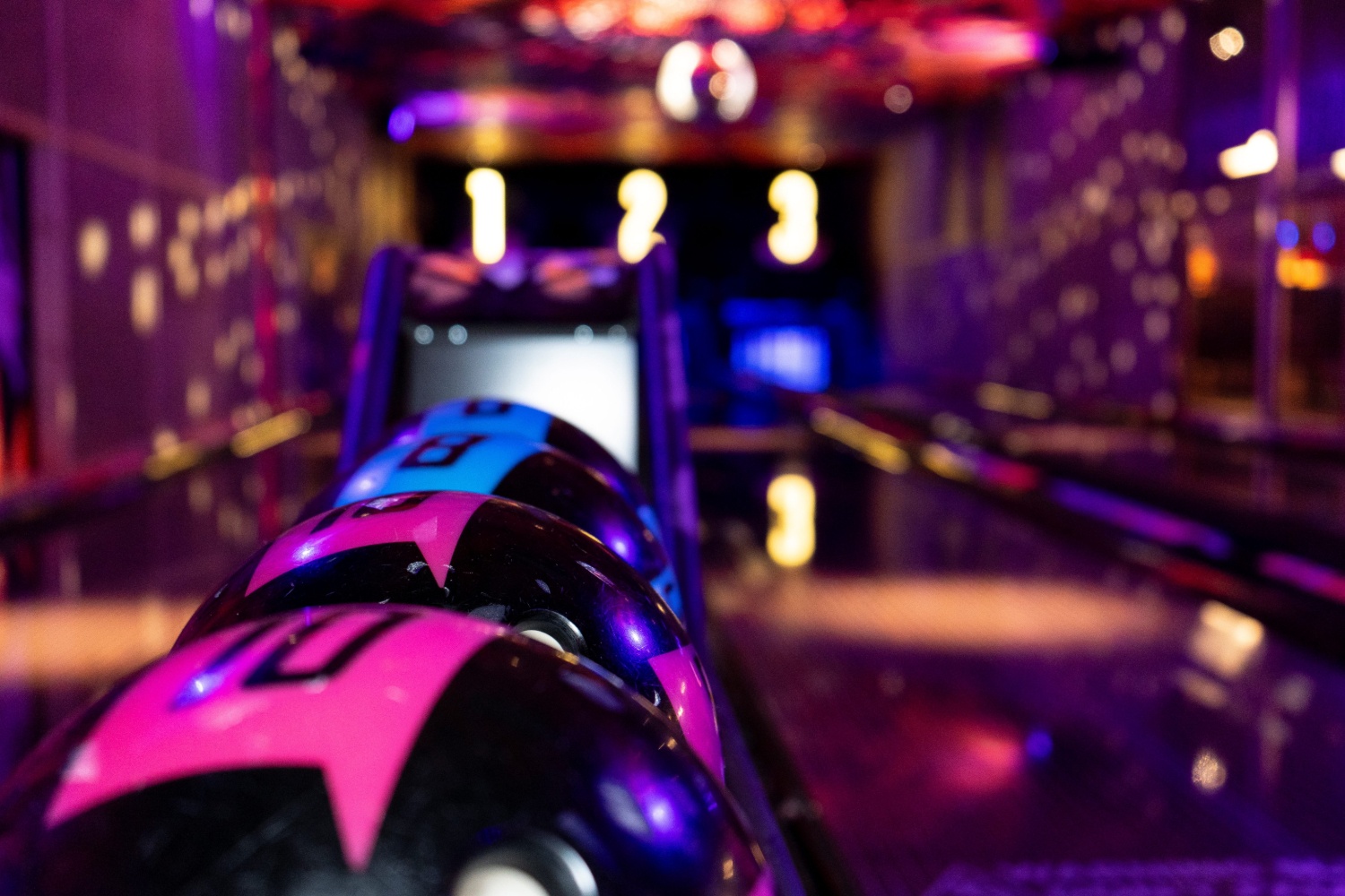 a close up of bowling balls at a lane with low lighting and bright neon lights
