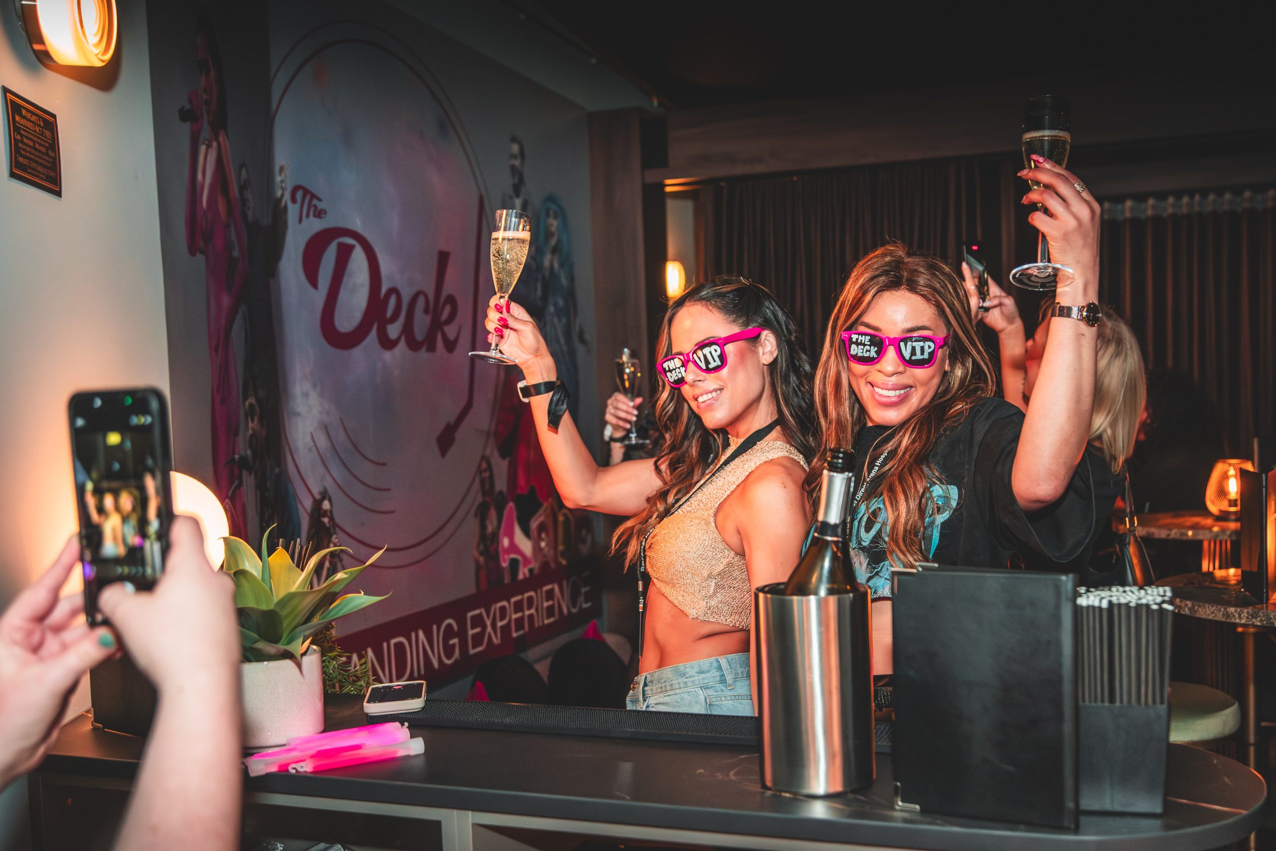 two people dancing with drinks in their hands and taking photos