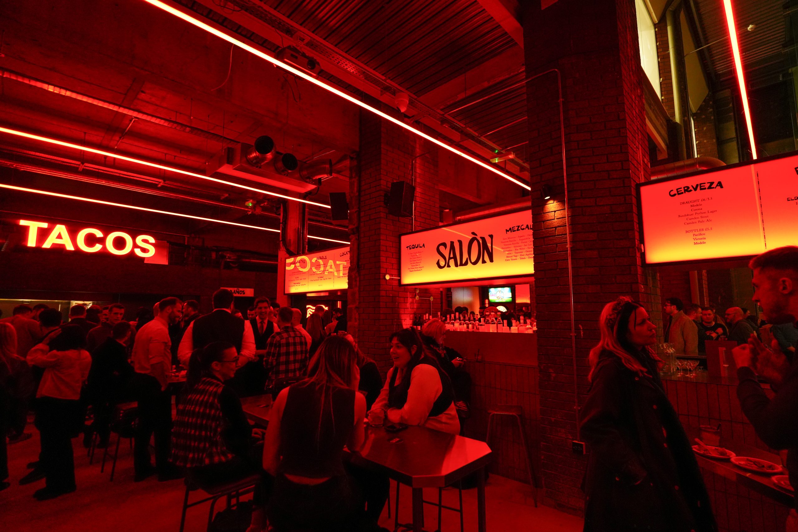 Interior view of Salon Madre bar and restaurant with people seated and red lighting.