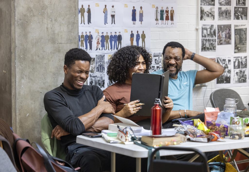 three people sat at a table filled with food, drinks and books