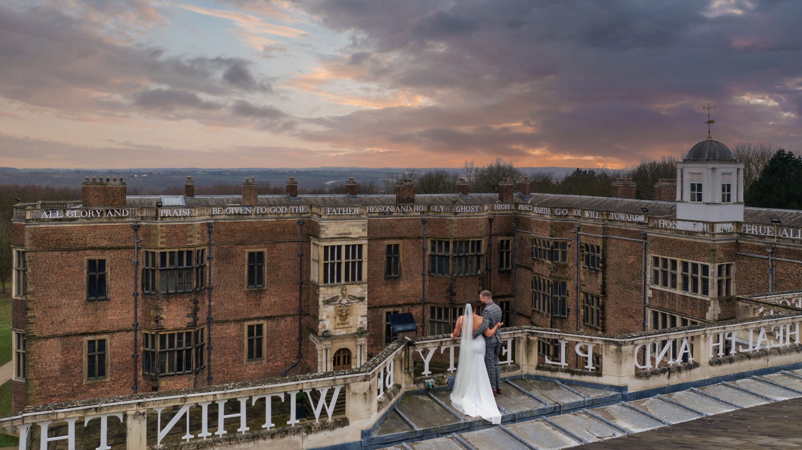 a bridge and groom stood on the rooftop at sunset of a historic building