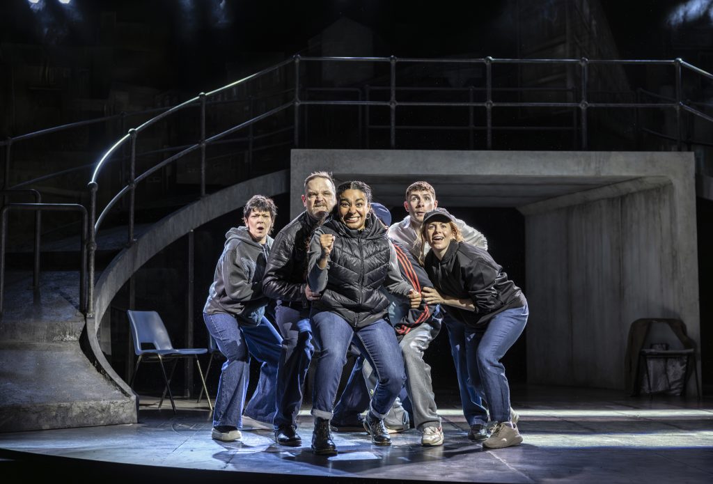 five people stood on a theatre stage looking at the audience