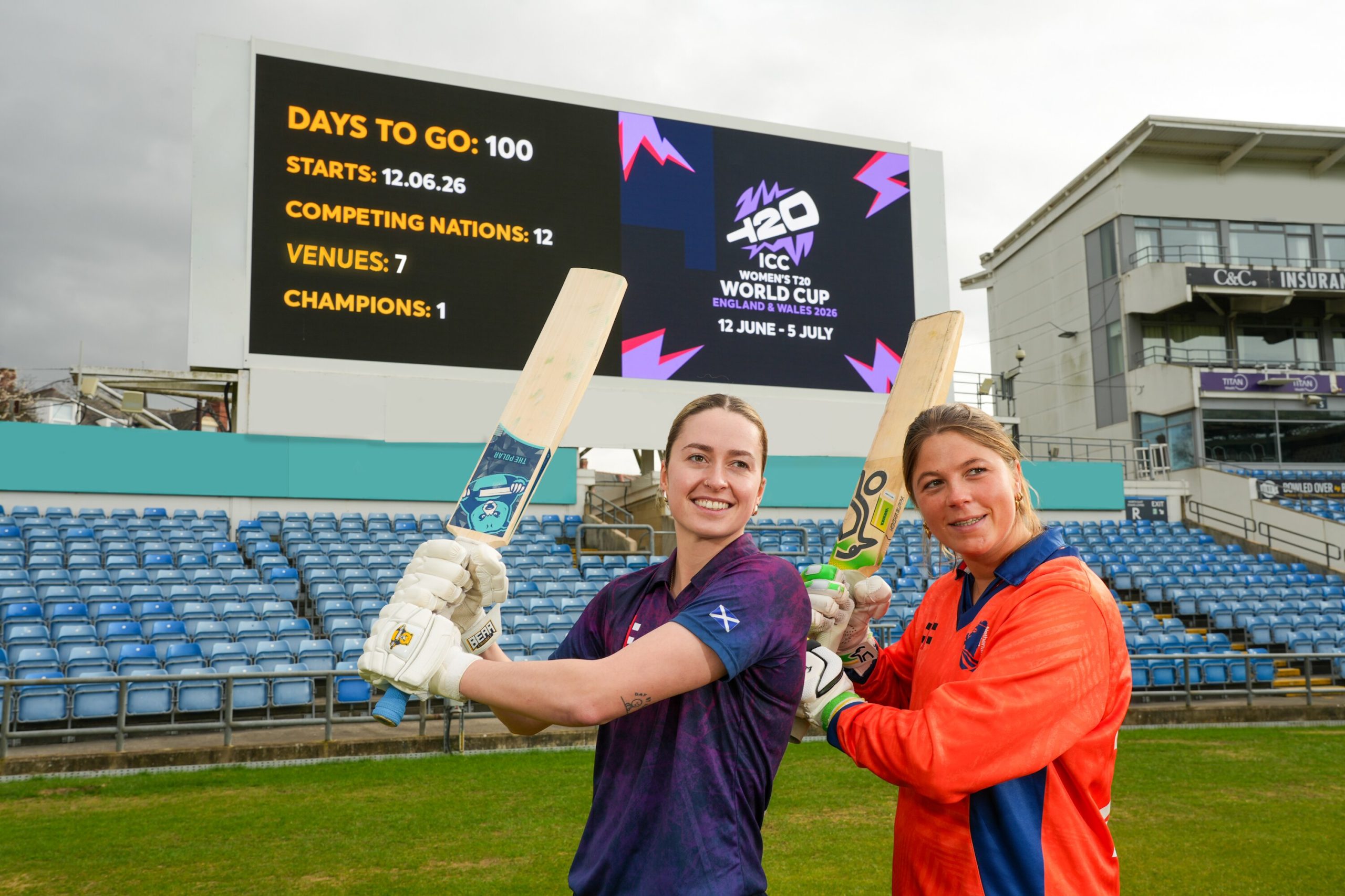 two women holding cricket bats in a stadium