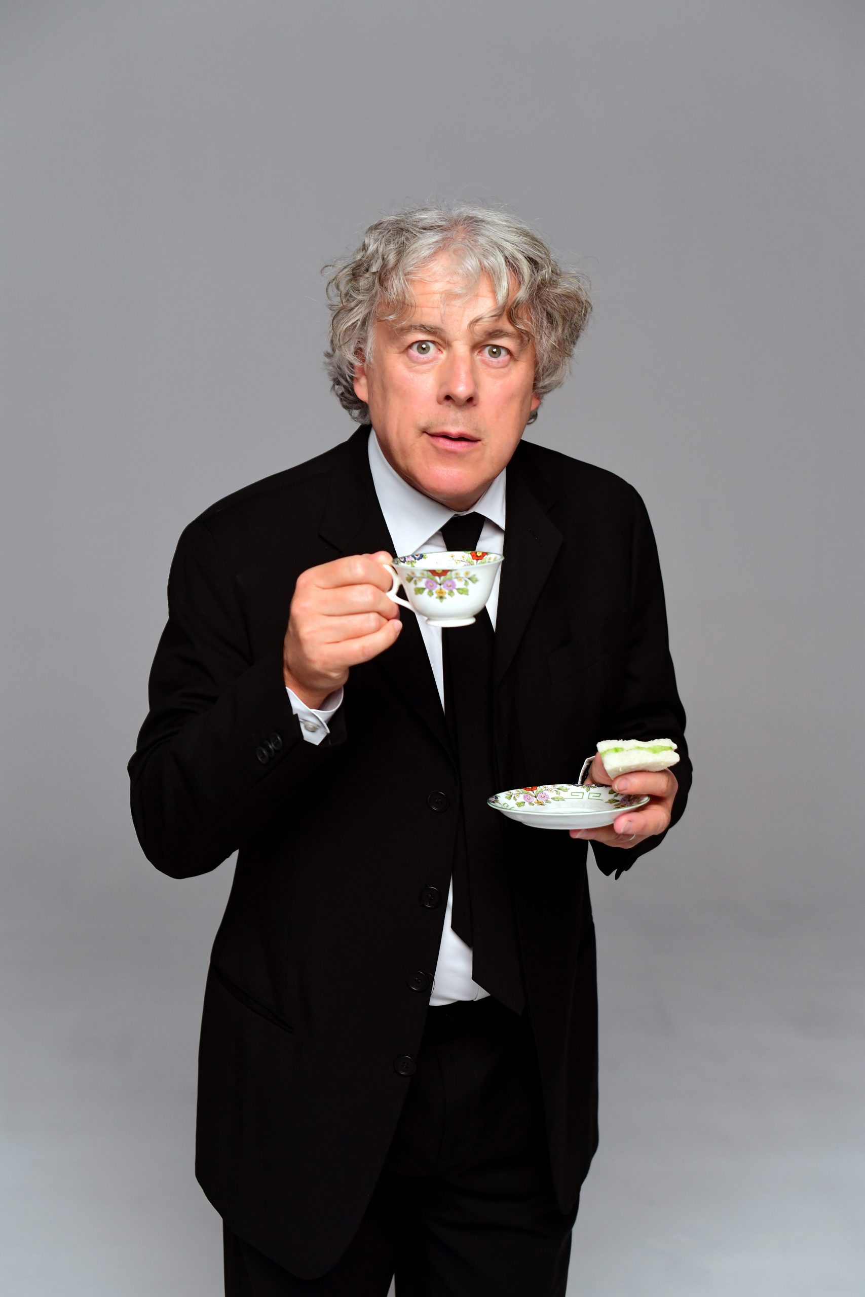 a man in a suit stood with a cup of tea and saucer