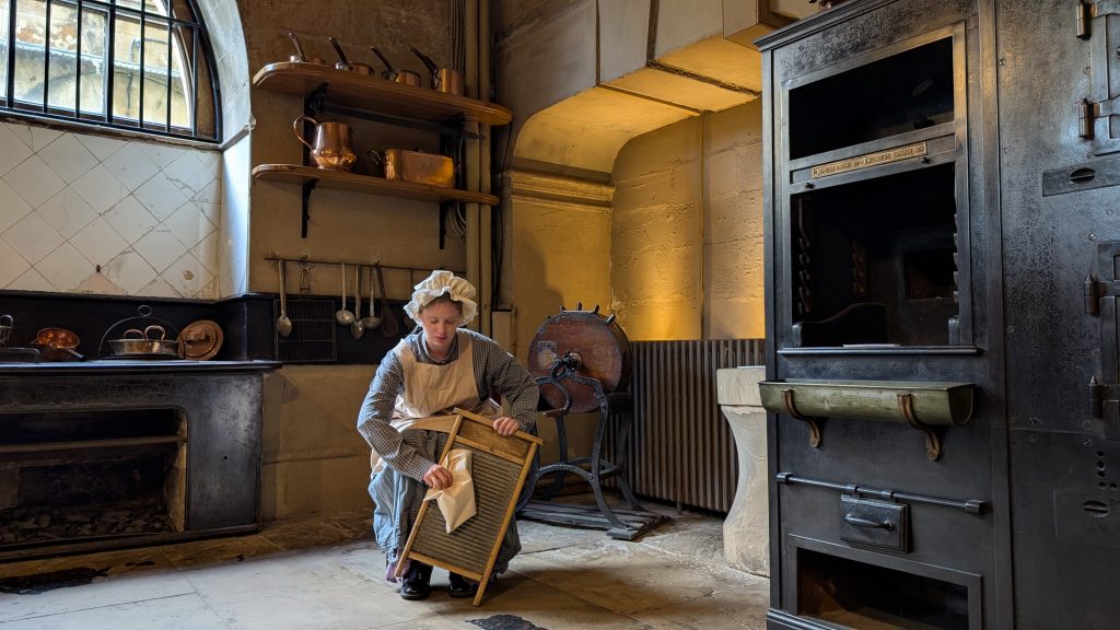 a large old kitchen and a woman dressed as a maid with an apron and cap on