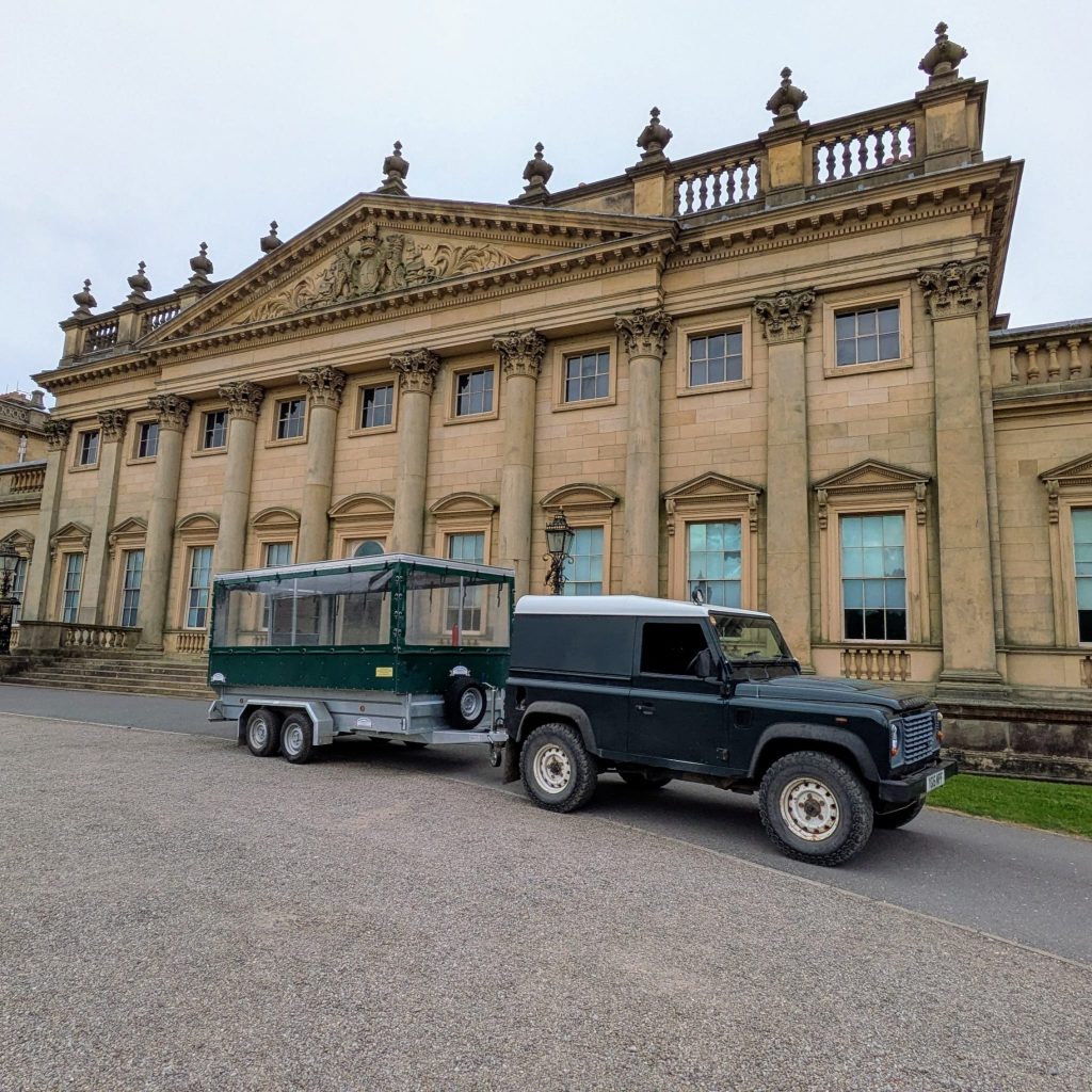 a large historic house with ornate front, and a vehicle with a trailer behind it