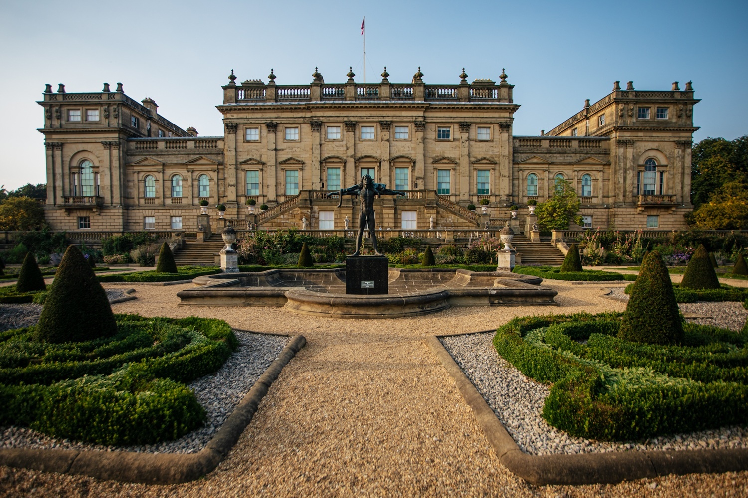 the exterior of a large historic house with curated gardens, statues and a water fountain