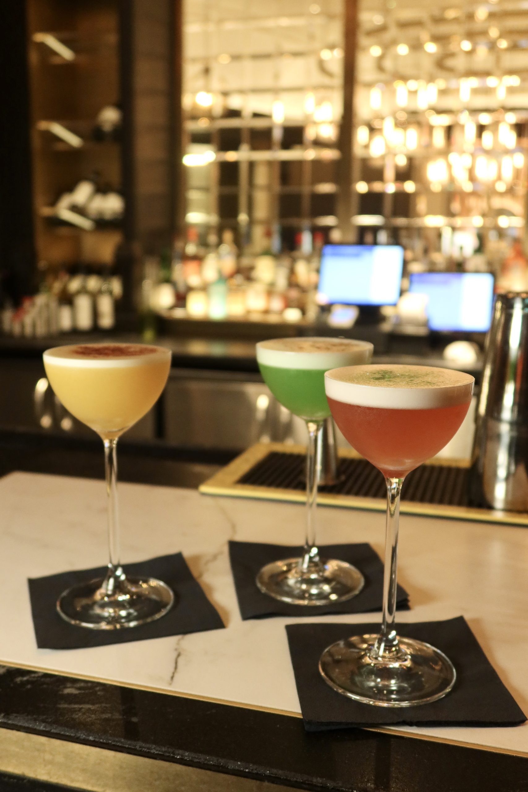 a bar with 3 tall cocktail glasses on top of different colours