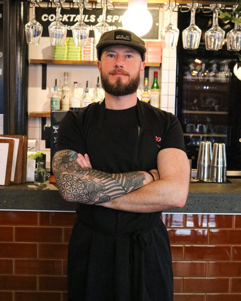 a man standing cross armed in front of a restaurant kitchen
