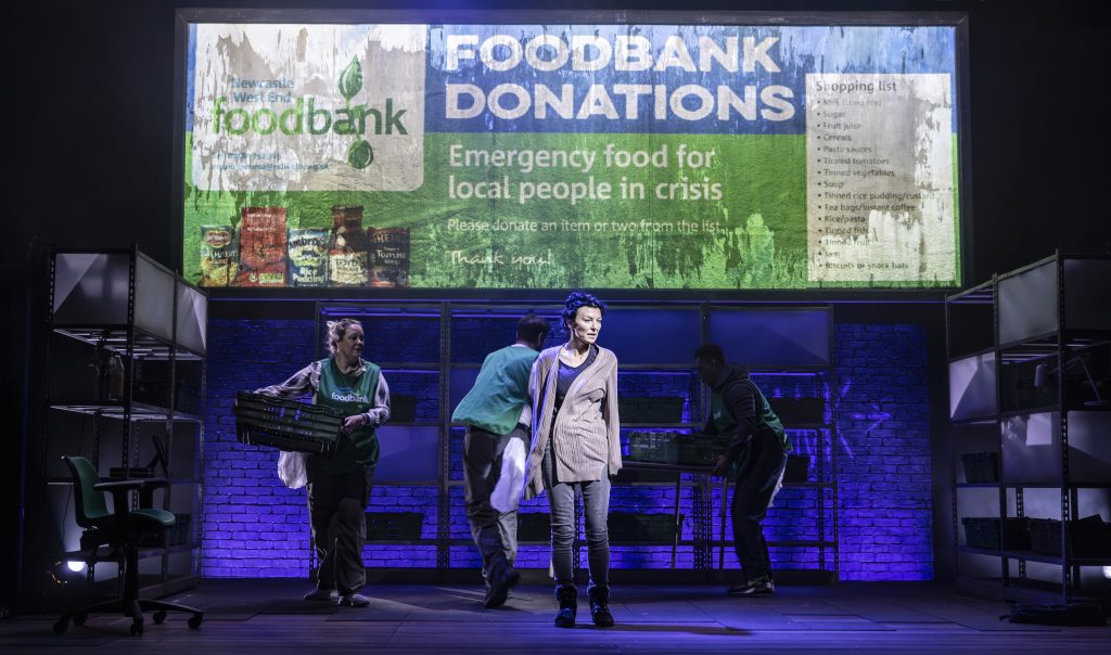 a theatre stage, several actors with a sign above them saying food bank