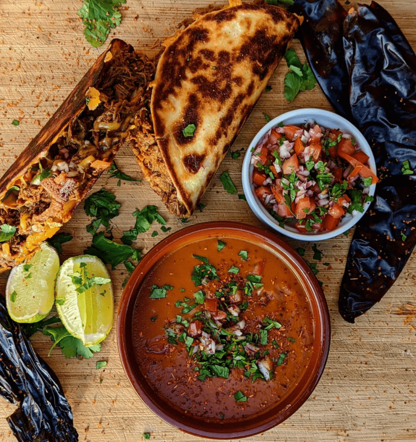 a top down view of a table with several bowls of food and some wraps with limes and garnish