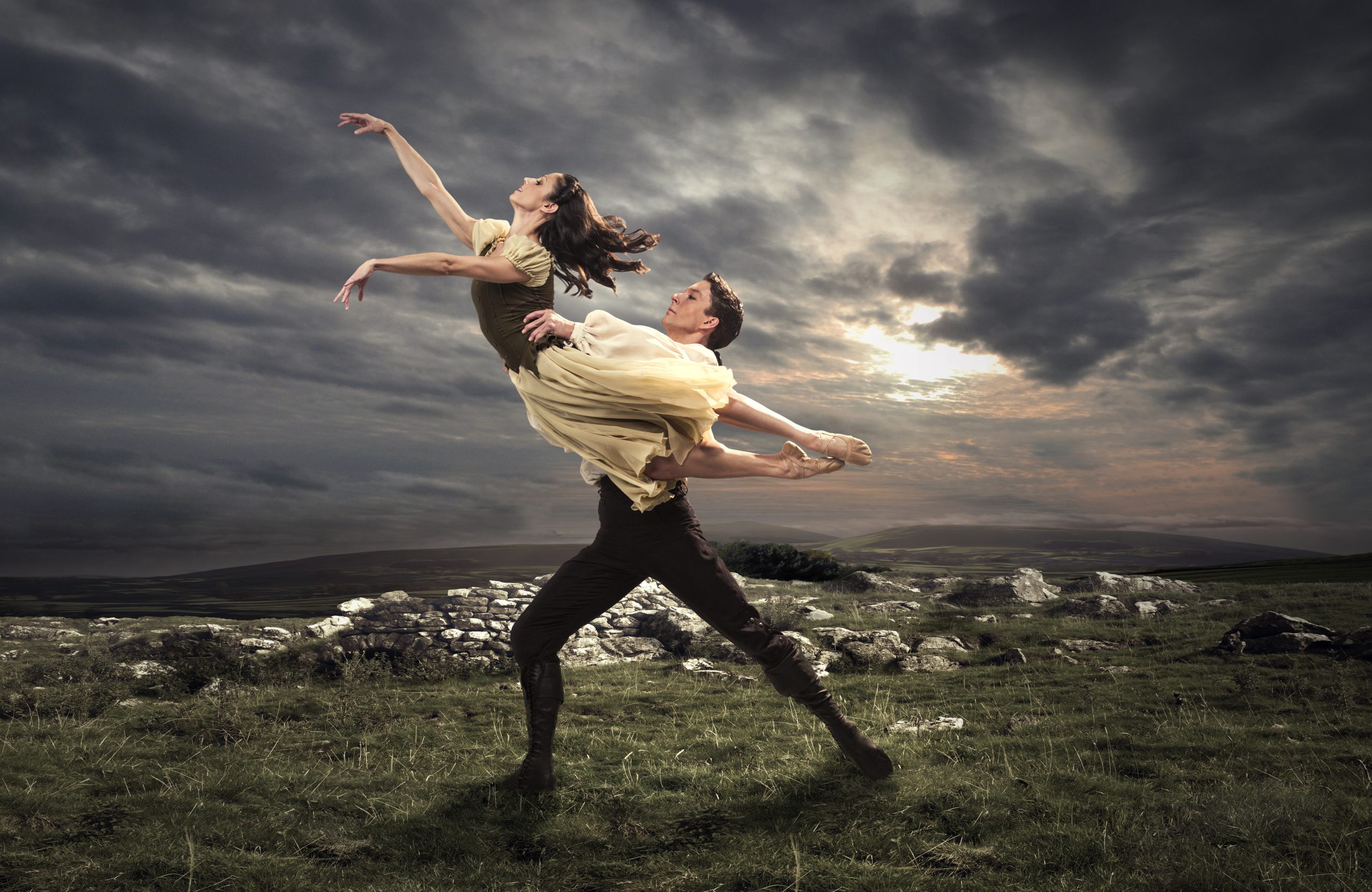 two ballet dancers posing with one being held up into air, with a moody landscape behind them