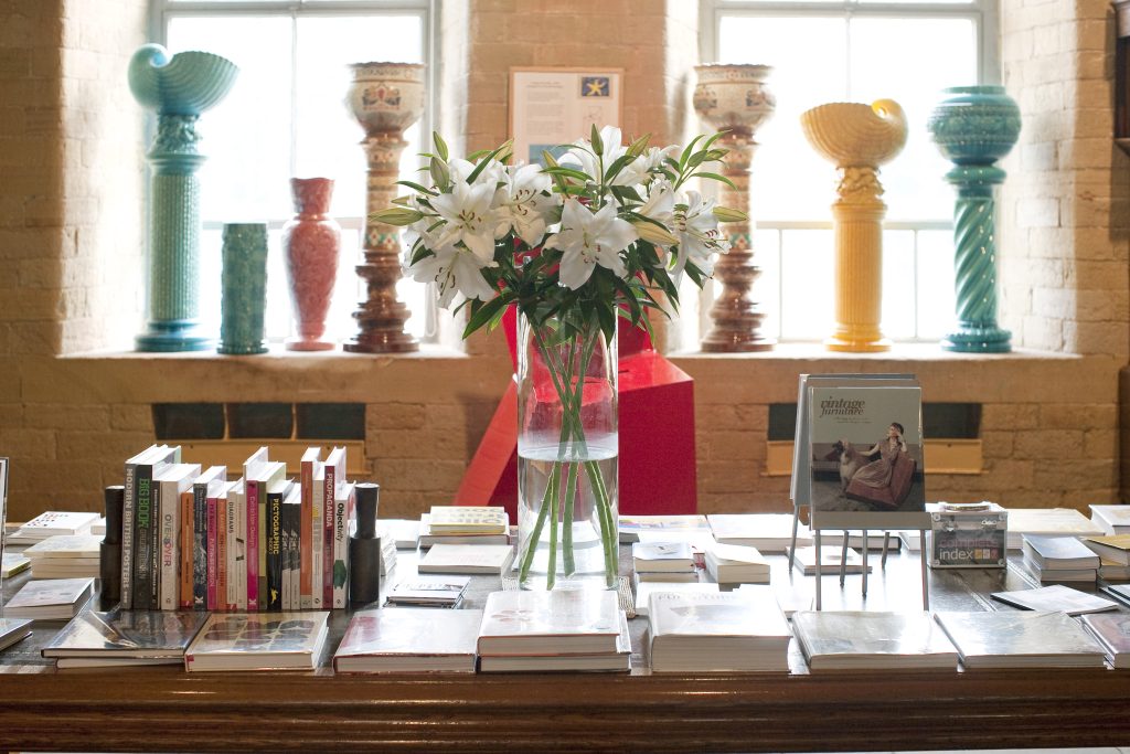 a table filled with books, vases and some more vases behind on a windowsill