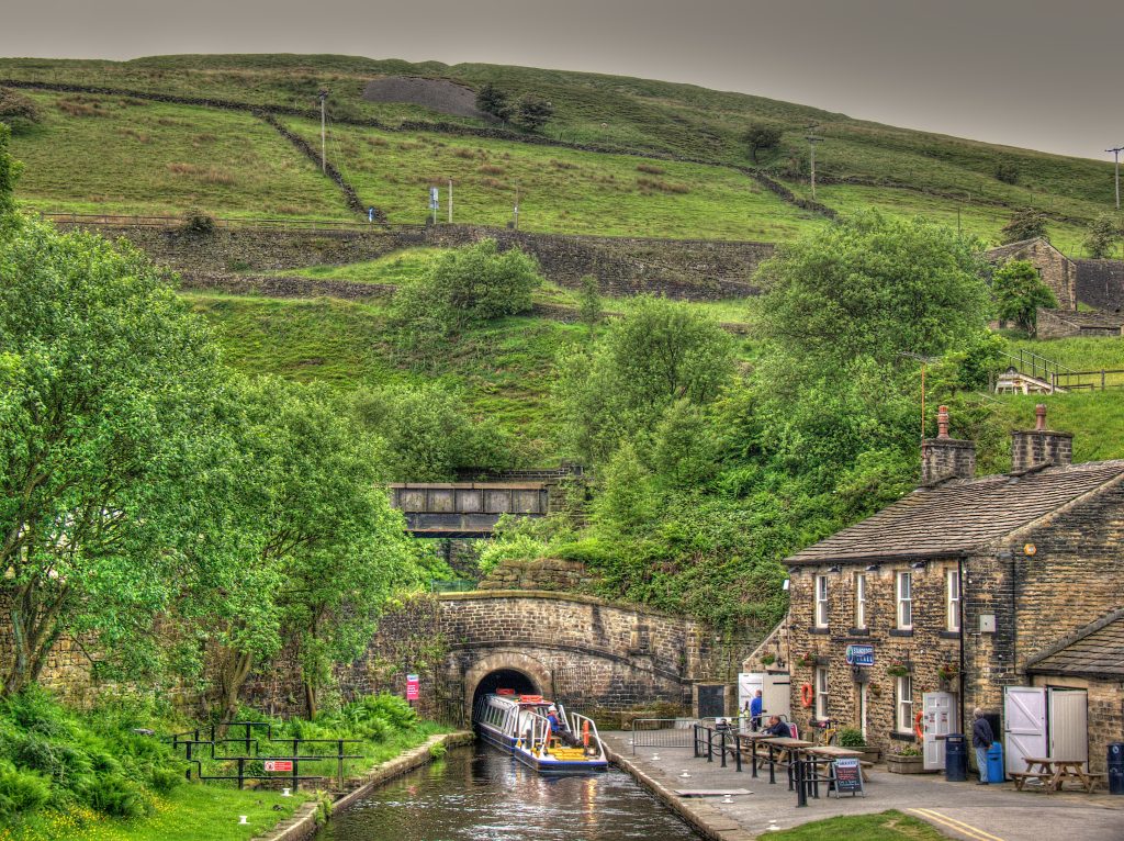 a view of the countryside and a canal boat going into a tunnel along the water