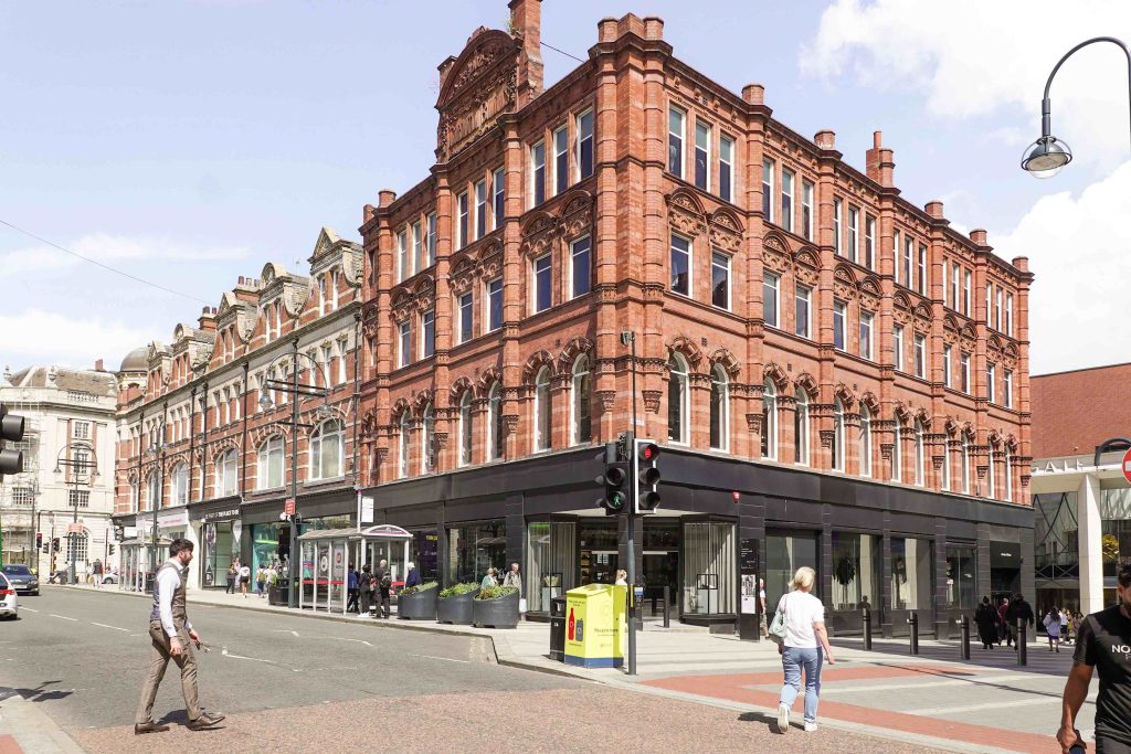 a large brick building next to a road, people crossing the road