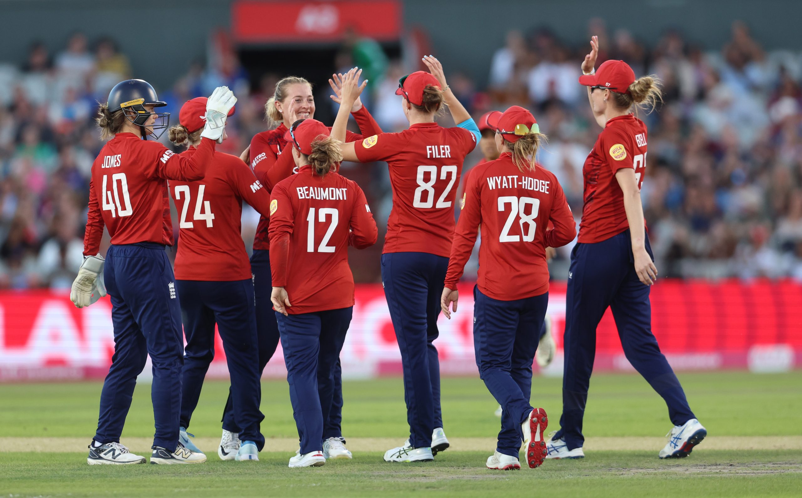 a team of female cricketers high fiving each other on a pitch