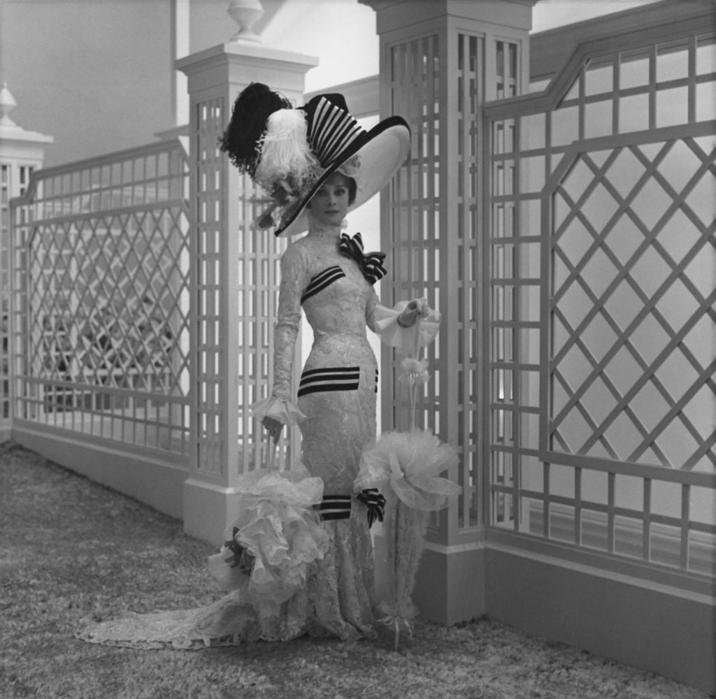 a black and white photograph of audrey hepburn in an ornate dress with a large hat with feathers