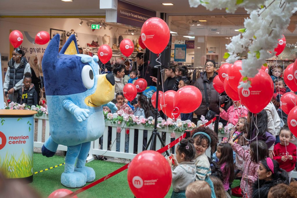 a crowd of children and parents watching bluey the dog perform surrounded by red balloons