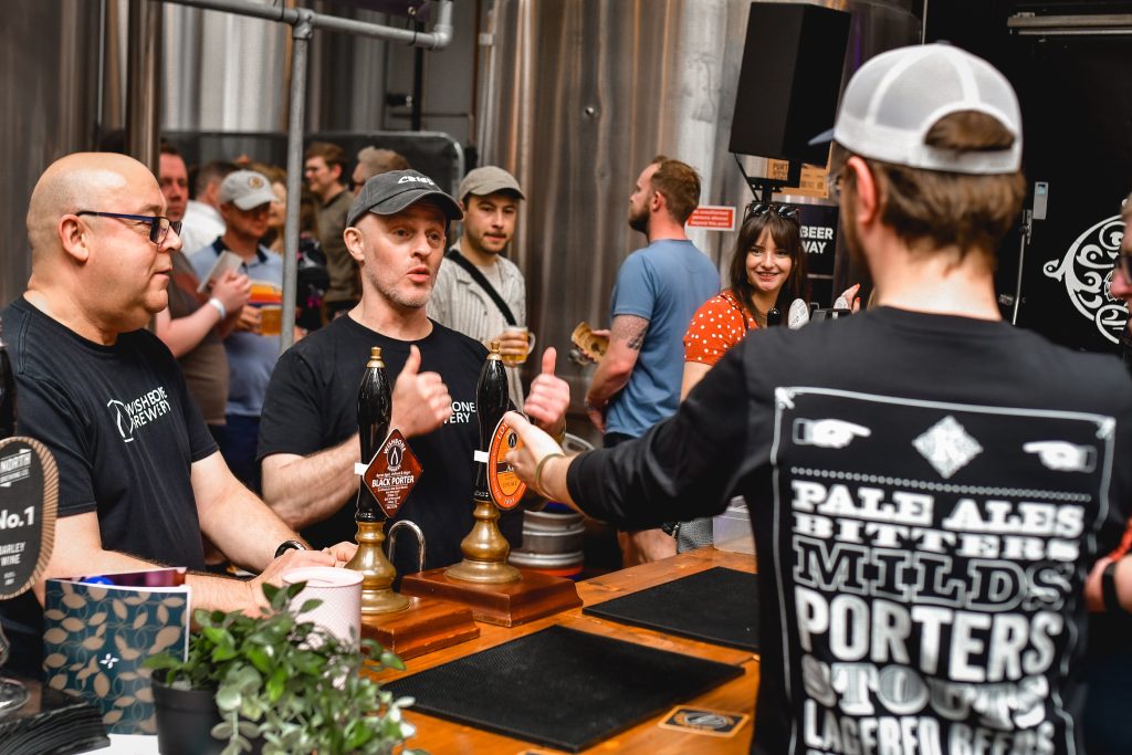 a crowd of people inside a bar with a person pouring a beer