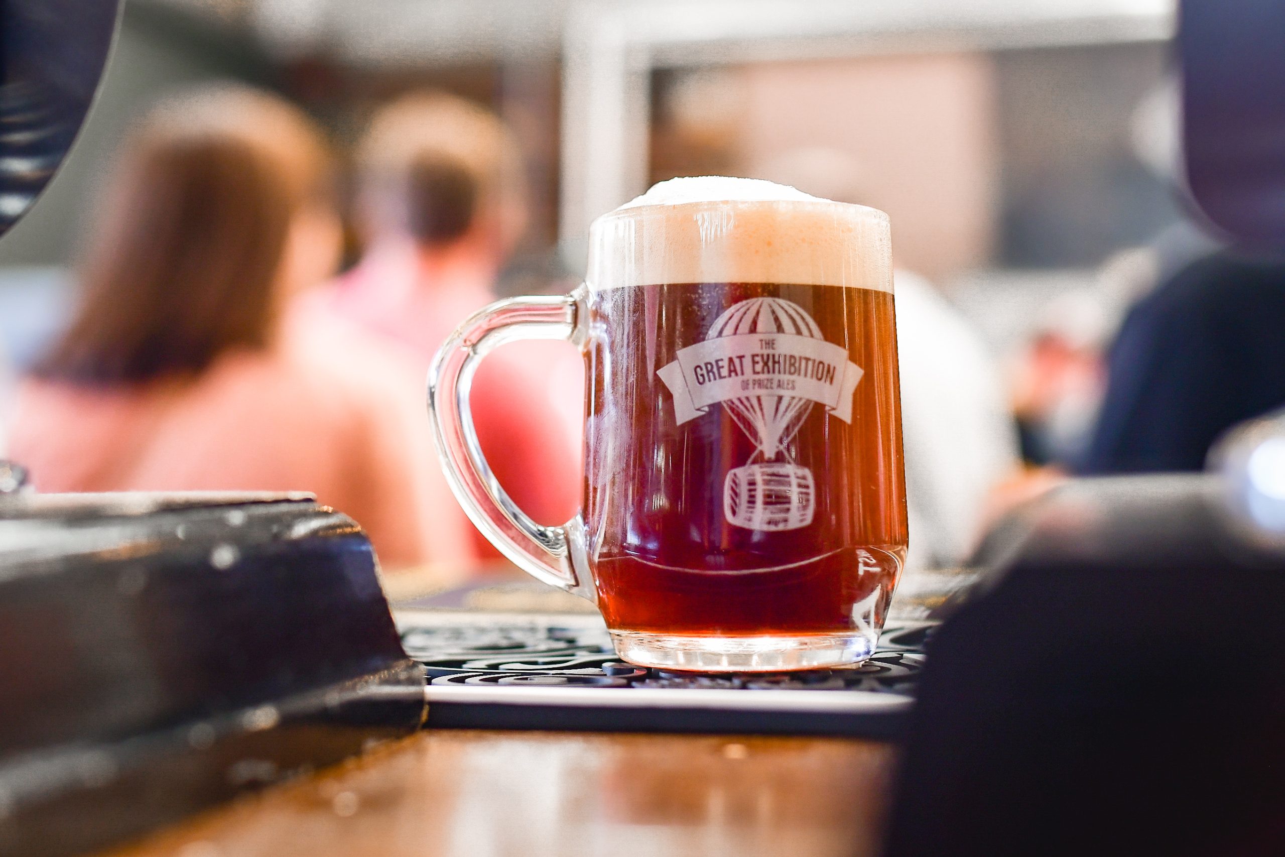 a glass beer jug on a counter in front of a crowd of people