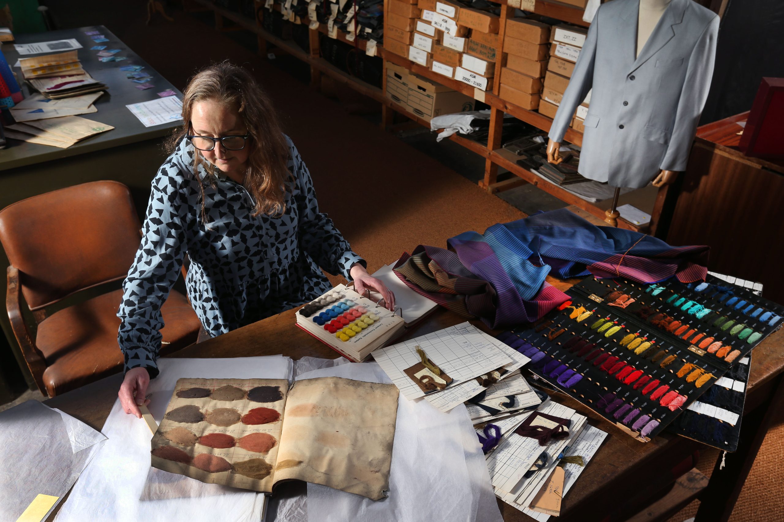a woman at a table filled with paints, sketchbooks and other art supplies