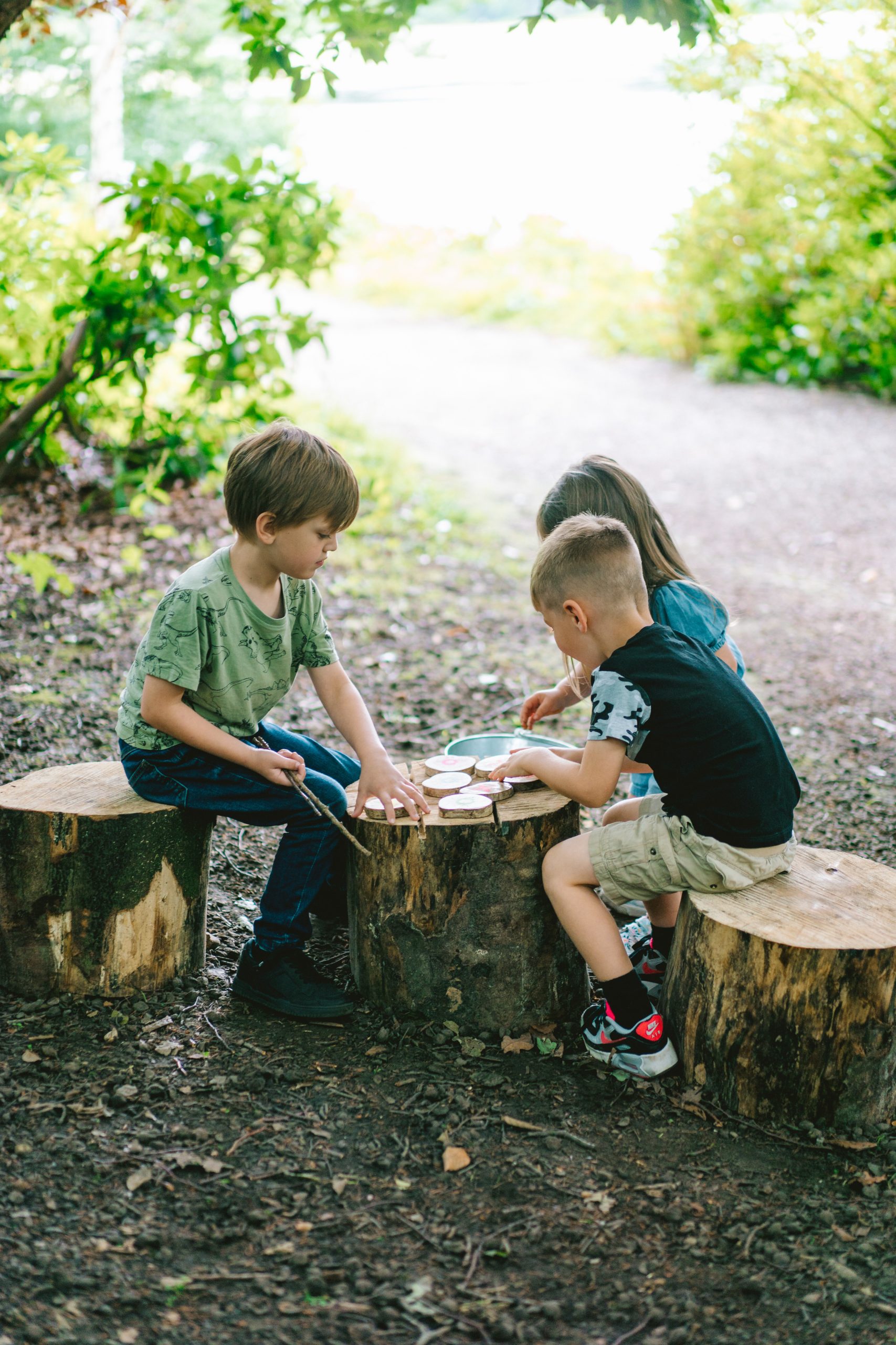 three children on some cut logs as tables and chairs in the middle of some trees