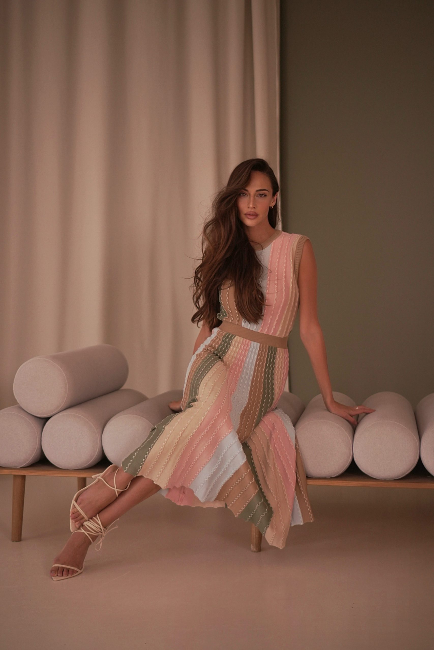 a woman with long hair and a colourful dress on sitting on a sofa looking at the camera